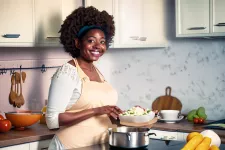 En glad kvinna står i kök och lagar mat. AI-generad bild (Adobe Firefly)/Janni Lundqvist Vedam. Foto.
