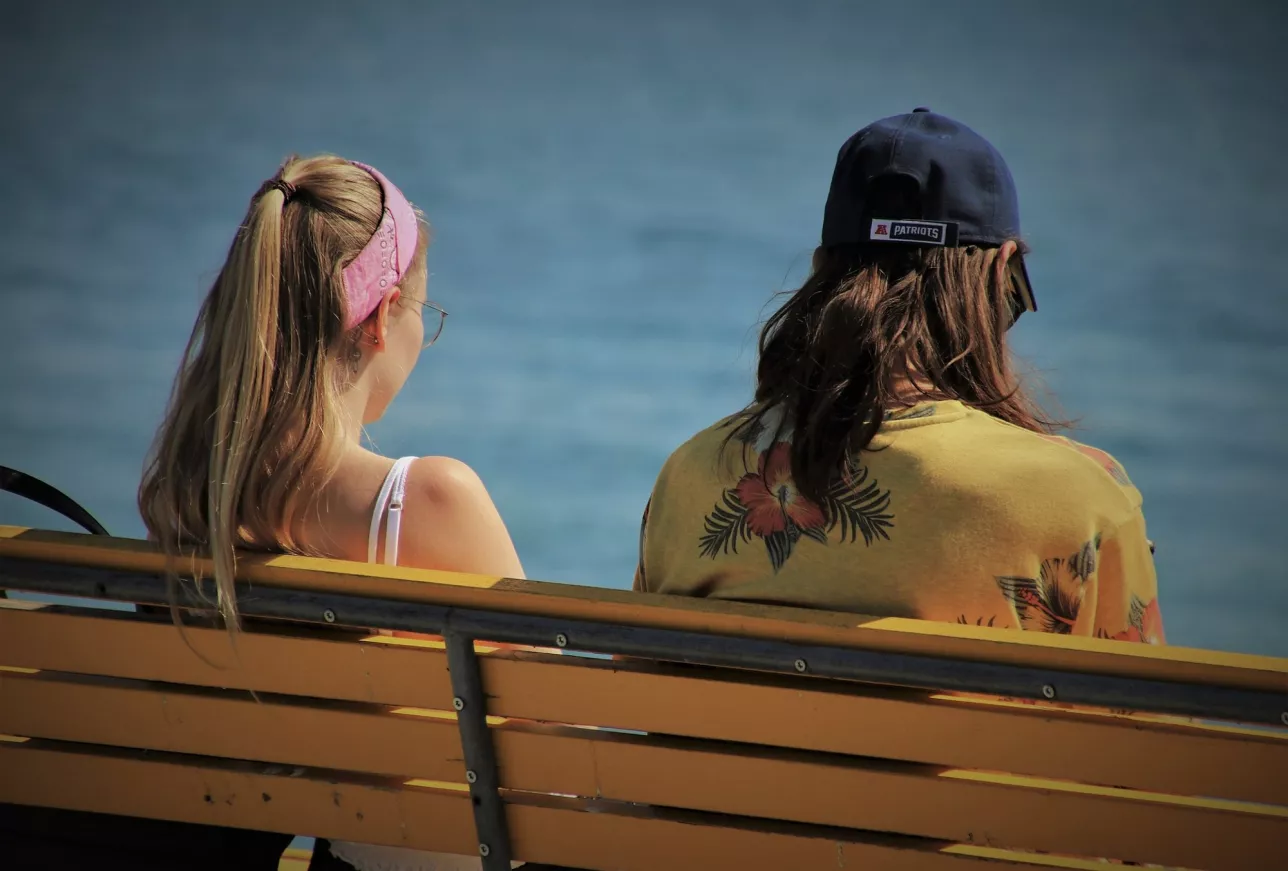Ung kvinna och man sitter på bänk vid havet i vårsolen