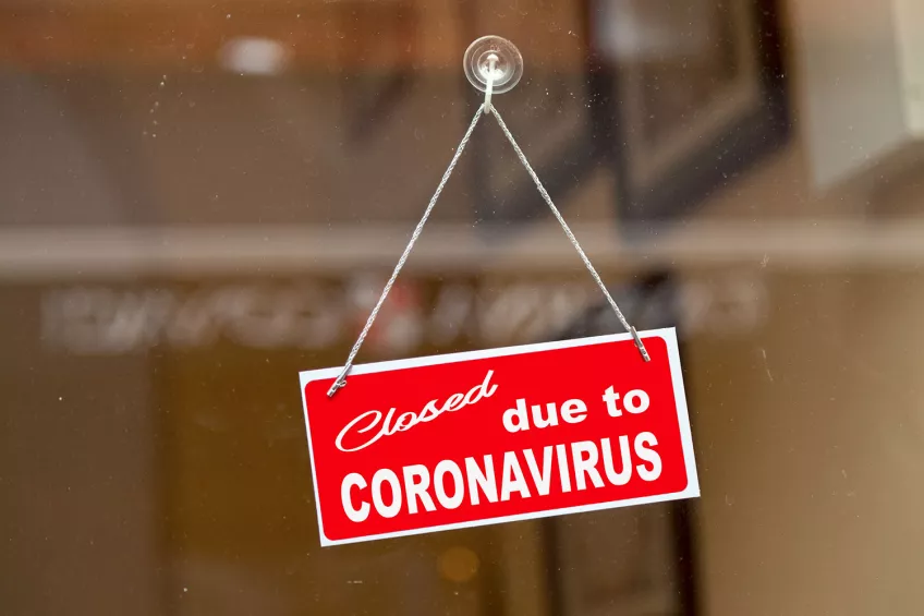 En röd skylt med den engelska texten för "stängt på grund av corona". Foto.