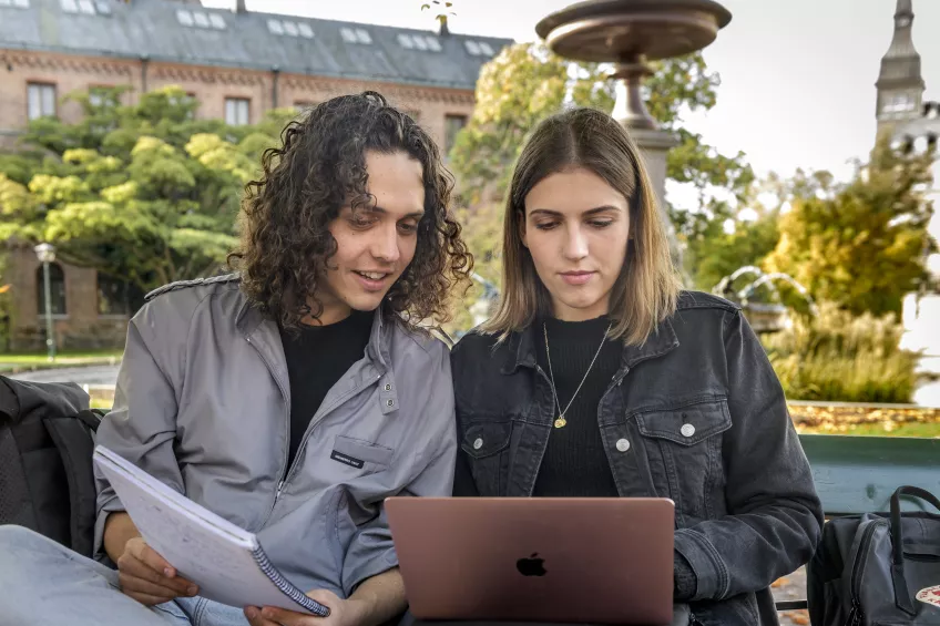Två studenter som sitter på en bänk och tittar på en dator tillsammans