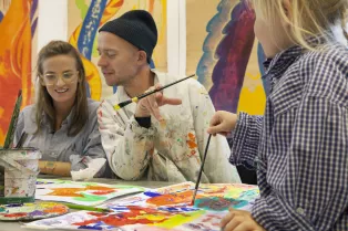 Studenter målar tillsammans vid ett bord med penslar och färg. Foto.