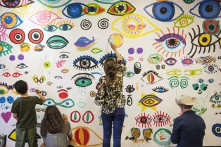 Människor i olika åldrar målar ögon på en vägg i olika färger. Foto.
